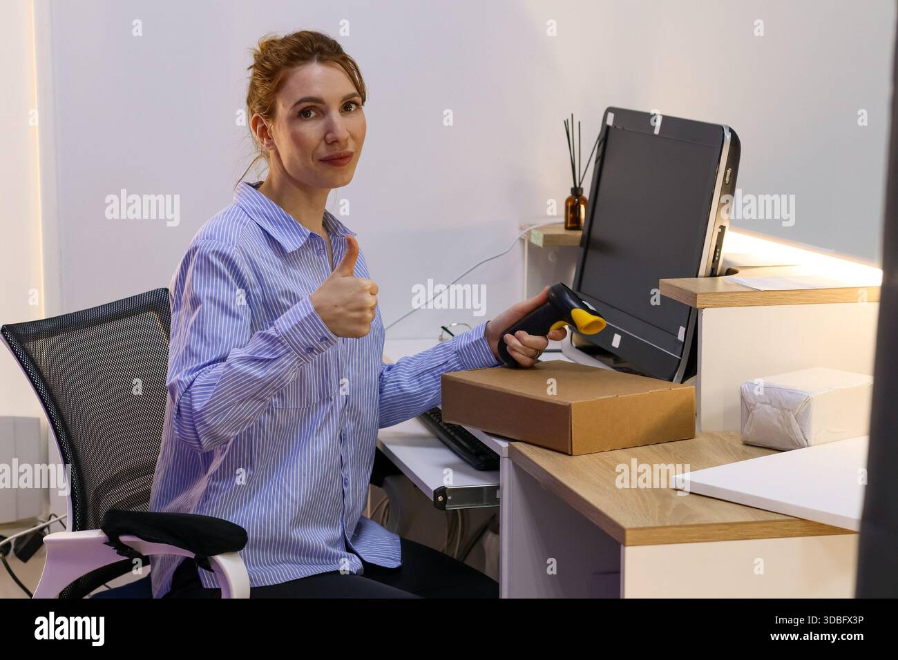 Il lavoratore del centro di evasione mostra lo strumento per il codice a barre vicino allo schermo e alle scatole del computer. Foto Stock