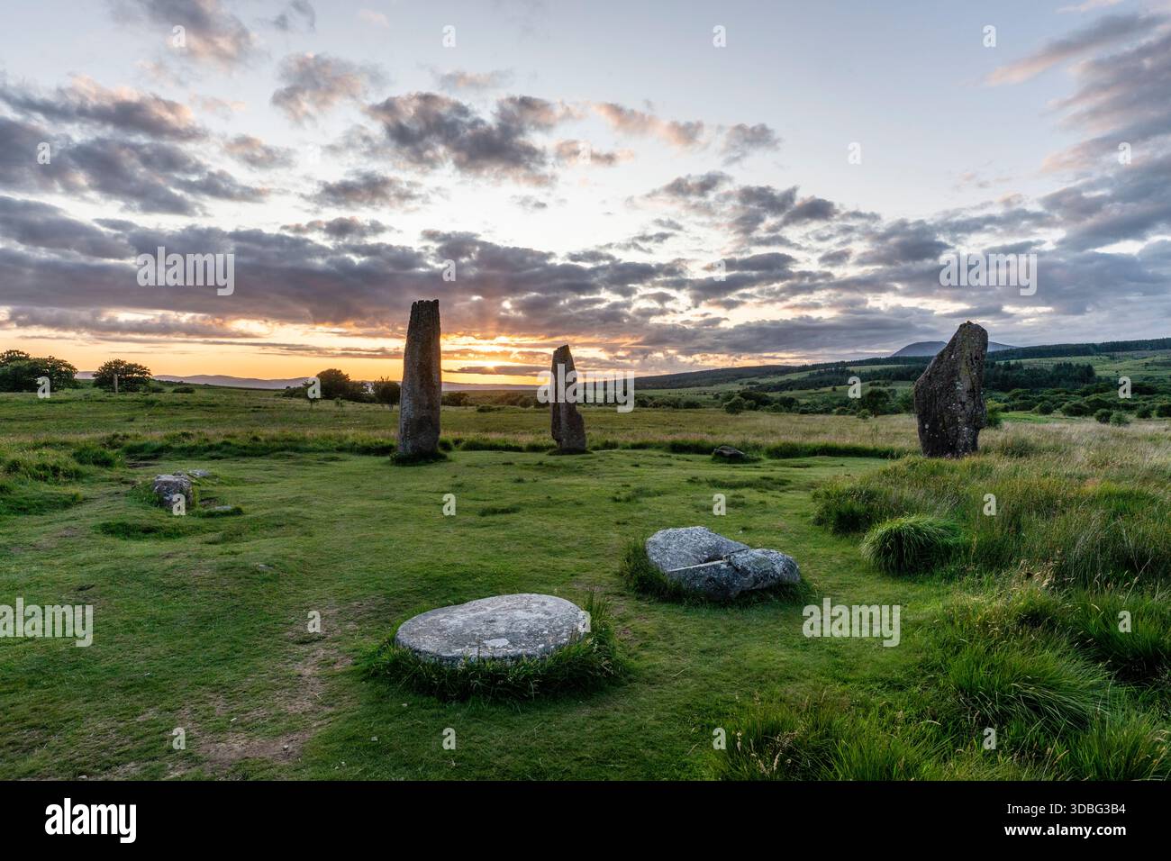 Il tramonto illumina un antico cerchio di pietra su una brughiera scozzese, con alte pietre erette, basse colline e erba verde in primo piano. Un luogo tranquillo e senza tempo Foto Stock