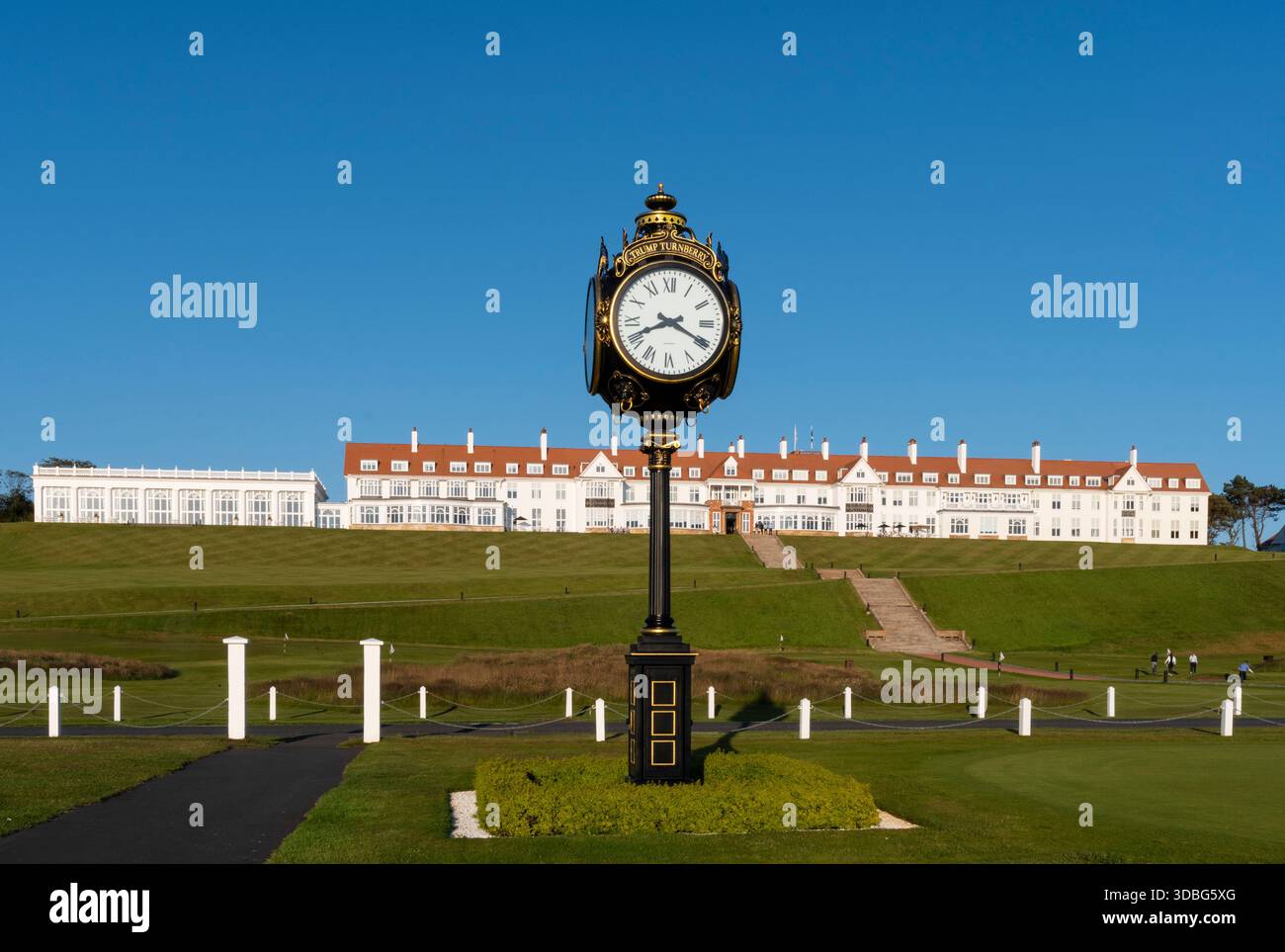 Elegante orologio ornato su un piedistallo con lo sfondo dell'hotel Turnberry e giardini curati. Foto Stock