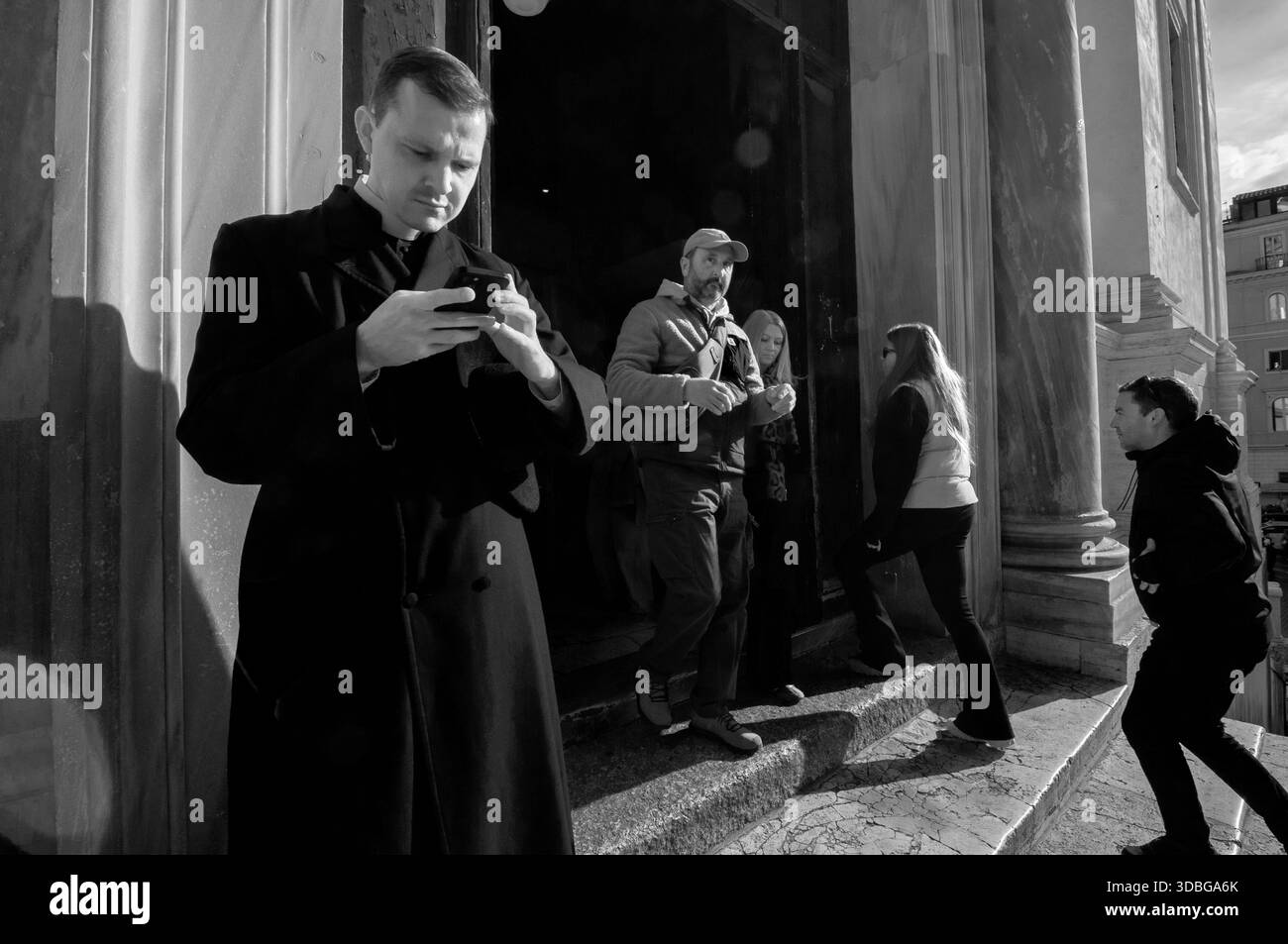 Un sacerdote con uno smartphone fuori dall'ingresso della Chiesa di Trinità dei Monti, Roma. Foto Stock