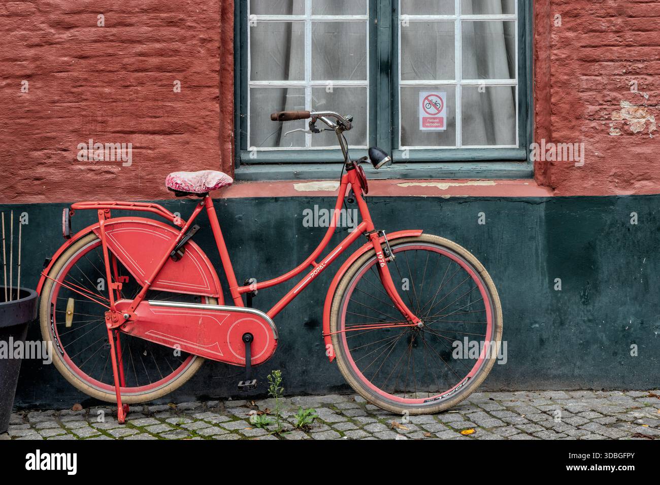 Vecchia bicicletta rossa di fronte a un muro rosso e nero nella storica città di Bruges, Belgio Foto Stock
