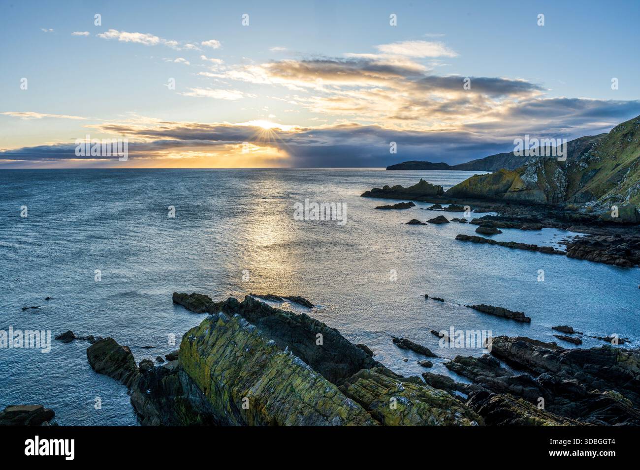 Il tramonto illumina la costa rocciosa scozzese con scogliere e mare calmo. Foto Stock