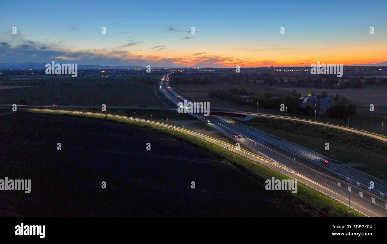 Traffico autostradale percorrendo l'autostrada A21 nei pressi di Piacenza Brescia di notte, veicoli che creano sentieri leggeri sulle infrastrutture e sulla rete stradale durante il sottopassaggio Foto Stock