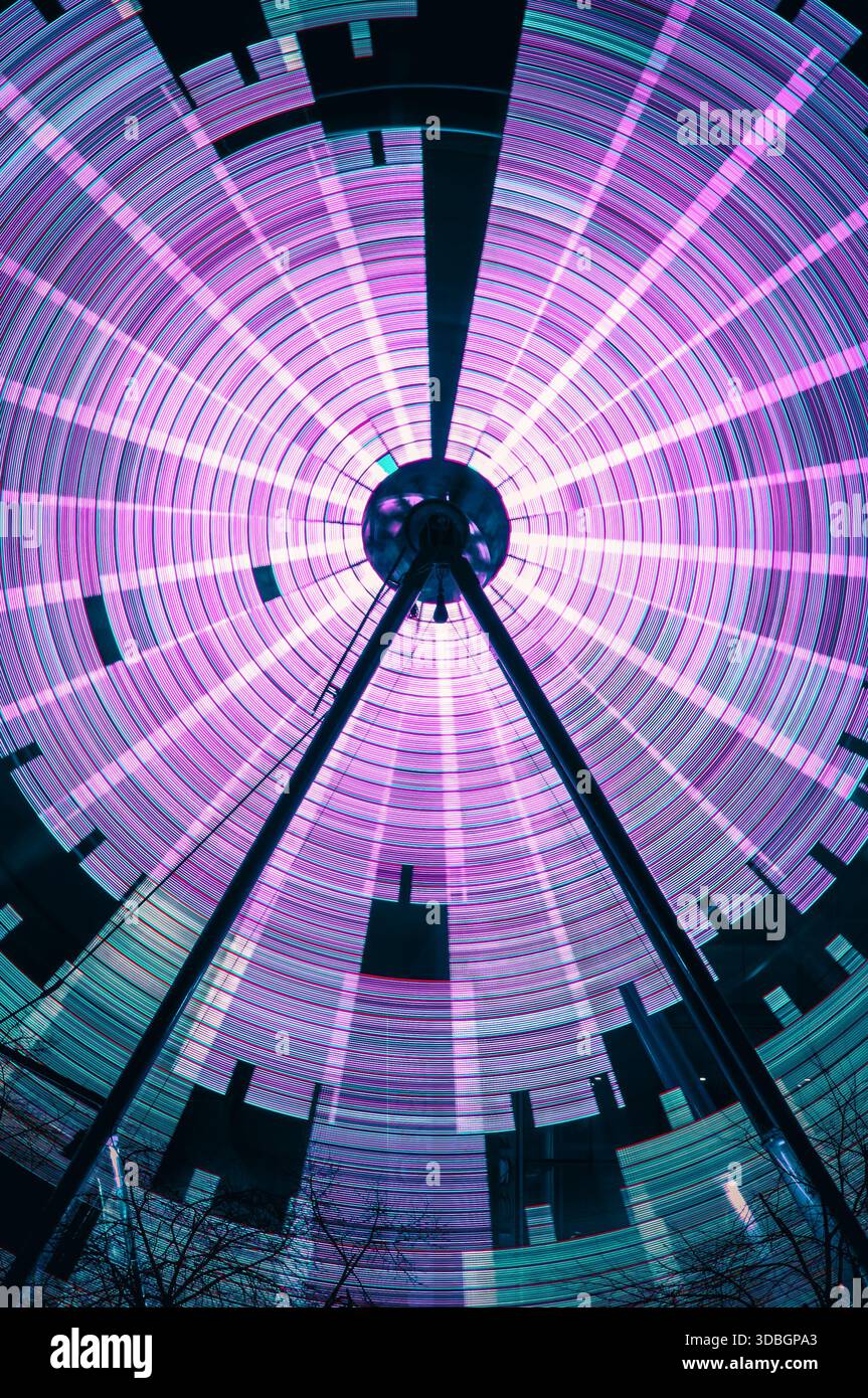 Scatto a lunga esposizione di una ruota panoramica in movimento al mercato invernale di Glasgow, che crea vivaci percorsi di luce circolare in rosa e verde acqua a partire dalle foto con otturatore lento Foto Stock