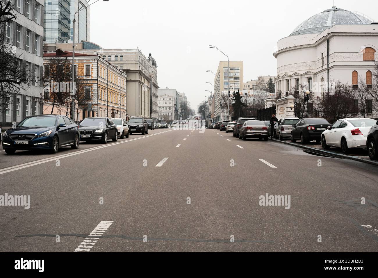 Una strada tranquilla fiancheggiata da auto parcheggiate ed eleganti edifici sotto un cielo grigio. Shevchenko Boulevard. Kiev, Ucraina. 16 dicembre 2025. Foto Stock