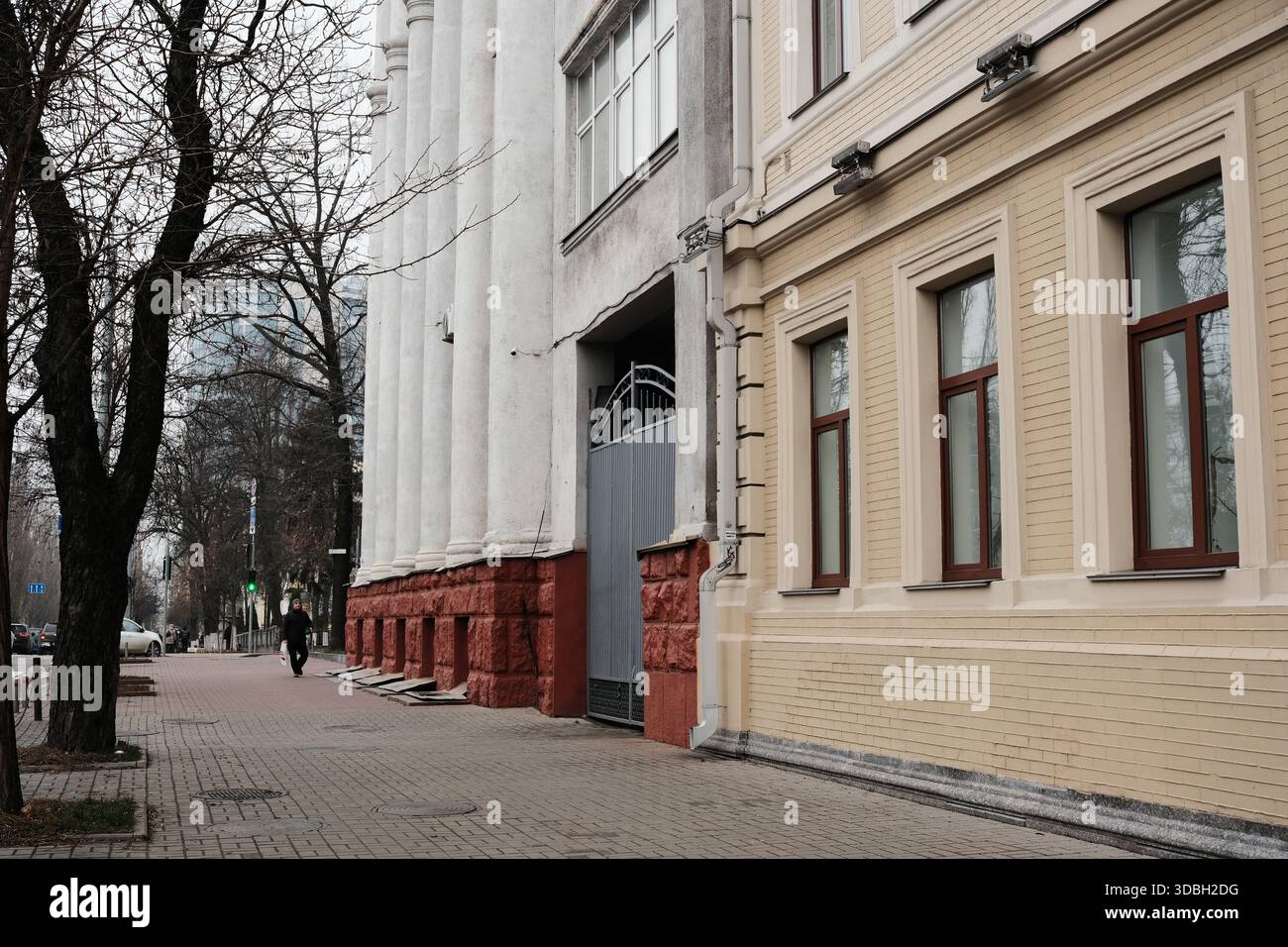 Una figura solitaria cammina davanti a un'elegante architettura in una strada tranquilla durante la primavera. Shevchenko Boulevard. Kiev, Ucraina. 16 dicembre 2025. Foto Stock