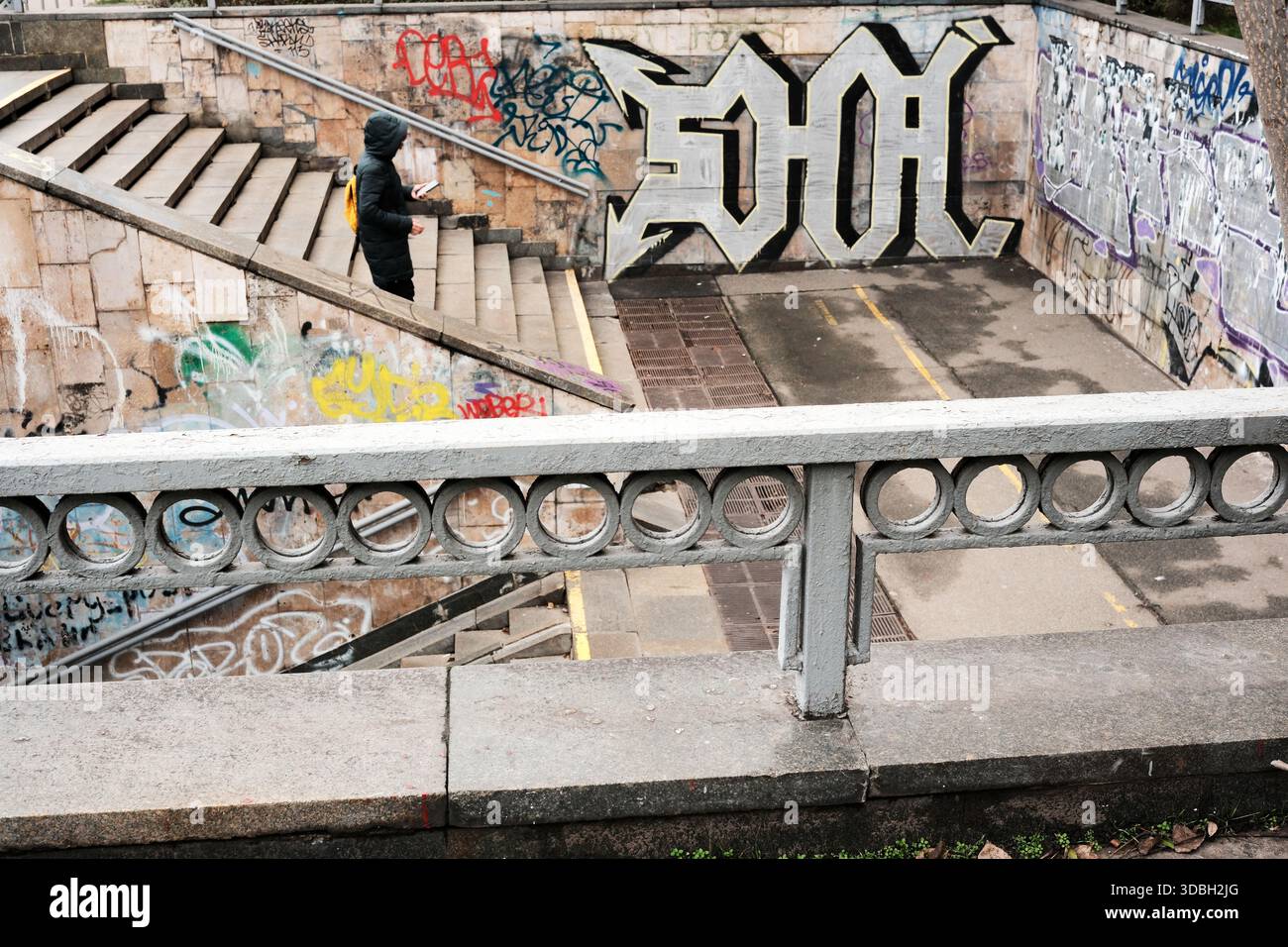 Una figura solitaria esplora vivaci graffiti su una scala in un ambiente urbano. Shevchenko Boulevard. Kiev, Ucraina. 16 dicembre 2025. Foto Stock