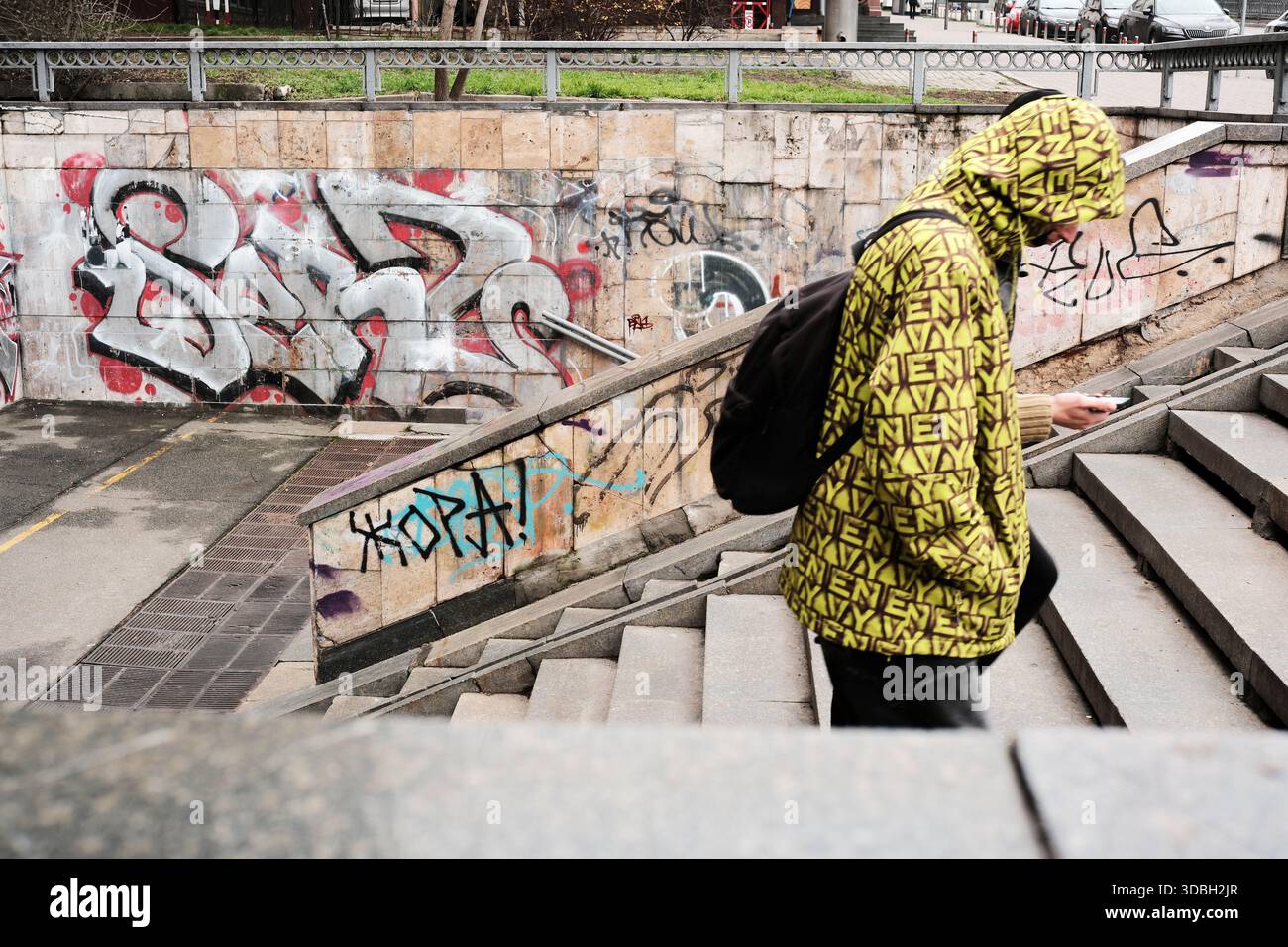 Un giovane con una felpa gialla brillante scende le scale, immerso nel telefono. Shevchenko Boulevard. Kiev, Ucraina. 16 dicembre 2025. Foto Stock