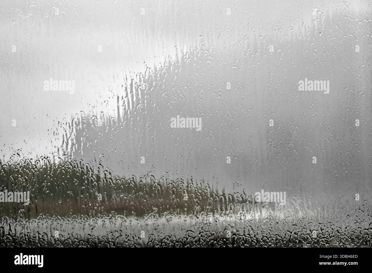 Primo piano di un vetro con pioggia intensa. Le goccioline d'acqua si estendono sul vetro, sfocando il mondo esterno in un acquerello soffice effe Foto Stock