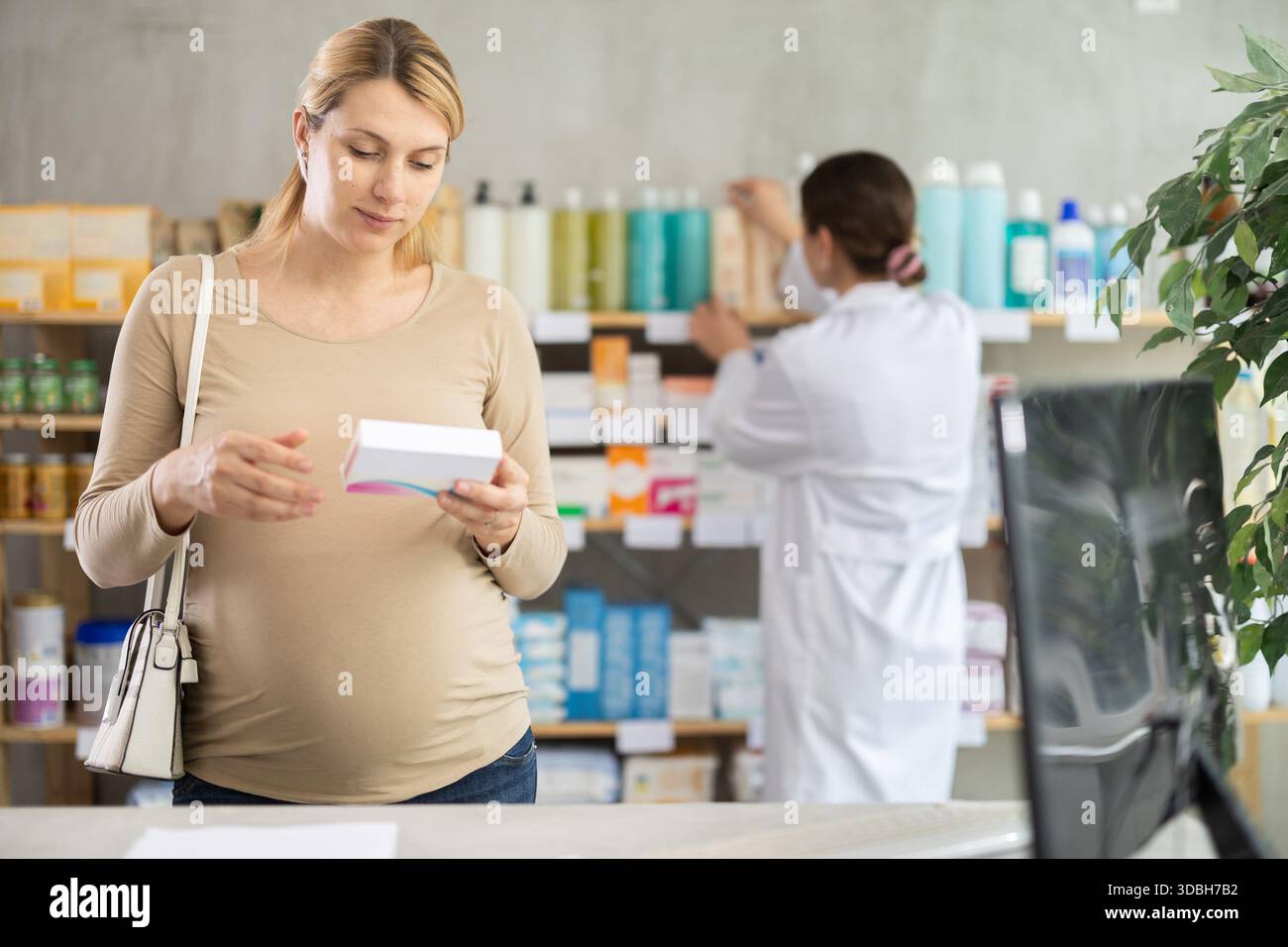 Donna incinta scegliere pillole di integratori in farmacia, lavoro del personale in background Foto Stock