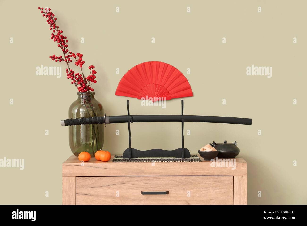 Katana con teiera, tè giapponese e decorazioni su comò vicino al muro verde. Festa di Capodanno Foto Stock