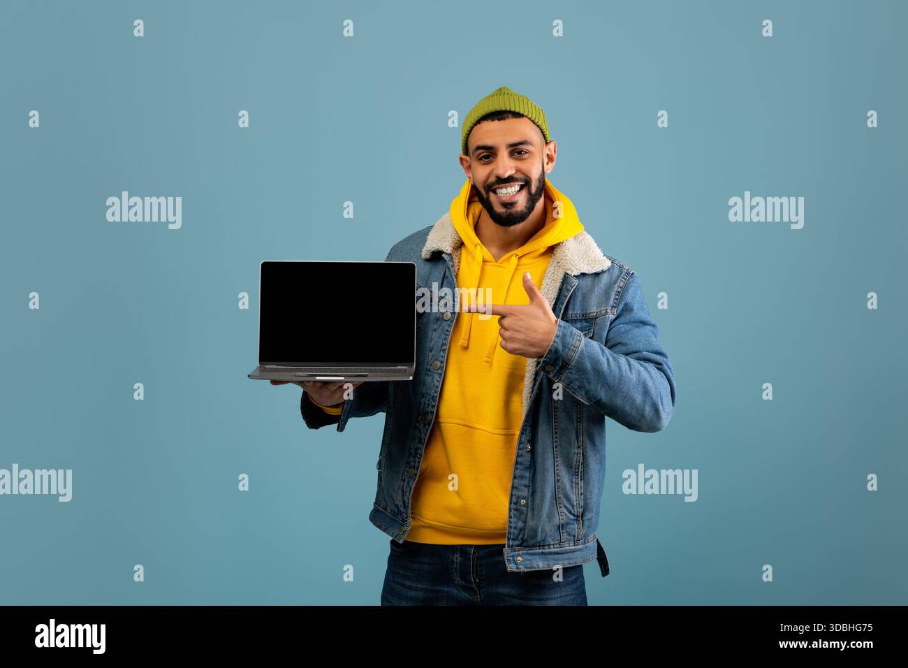 Young Man sfoggia un notebook su sfondo blu con un abbigliamento casual Foto Stock