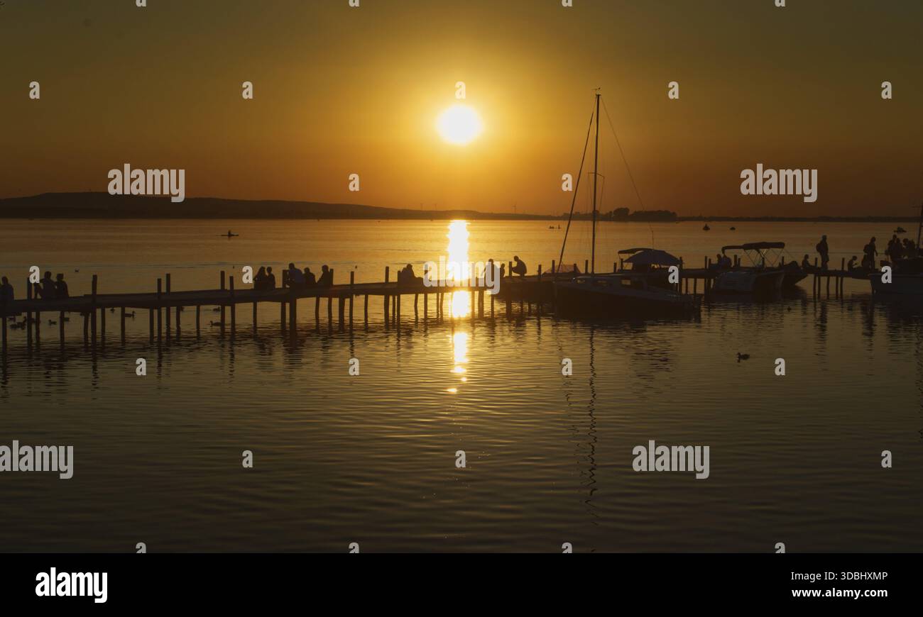 Tramonto sullo Steinhuder Meer con gente su un molo, che riflette le barche a vela, tranquillo, Steinhude Foto Stock
