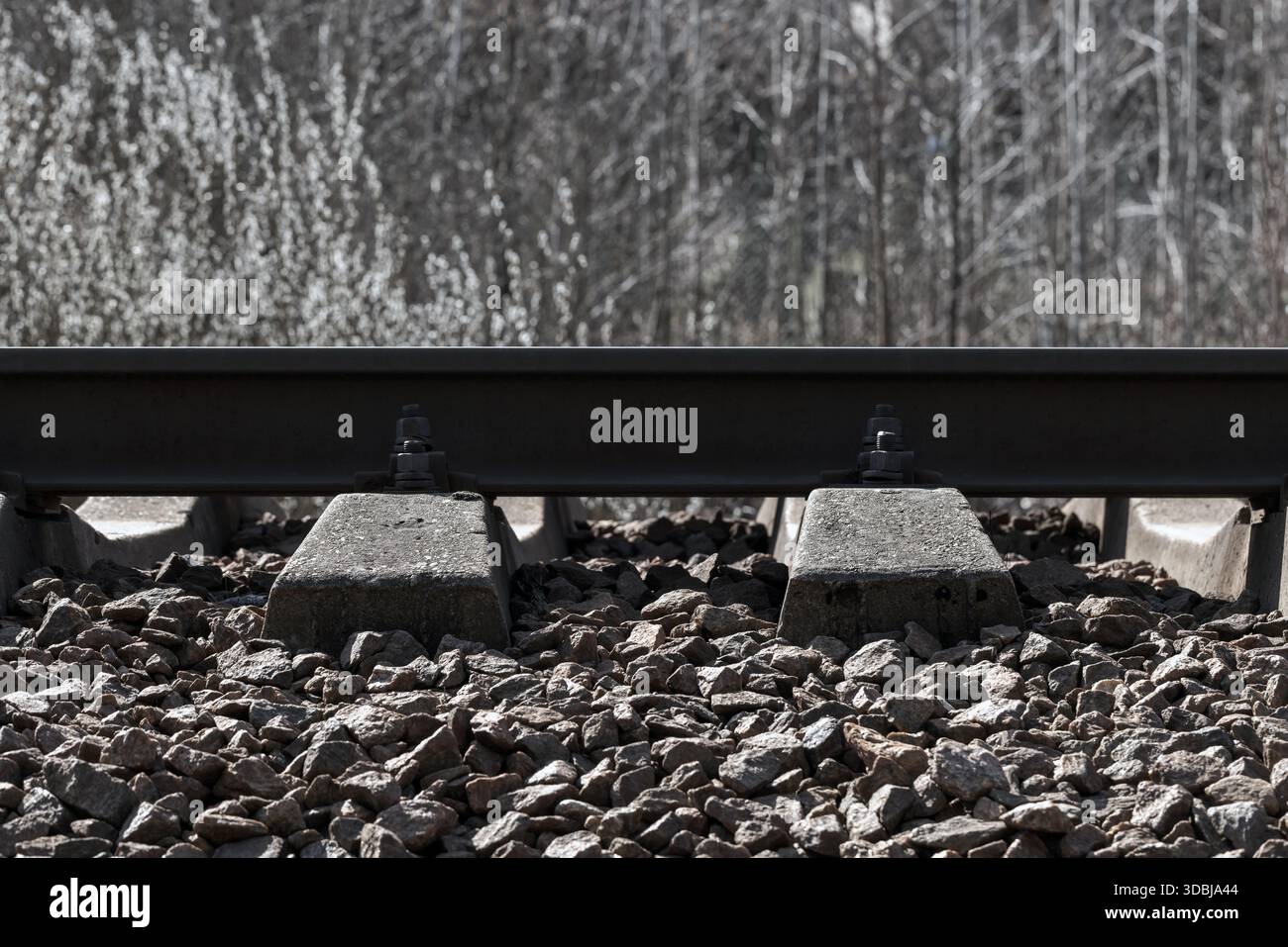 Una vista ravvicinata di un binario ferroviario mostra traverse in cemento, rotaie in acciaio e un letto di ghiaia. L'immagine trasmette l'infrastruttura industriale, la durata, Foto Stock