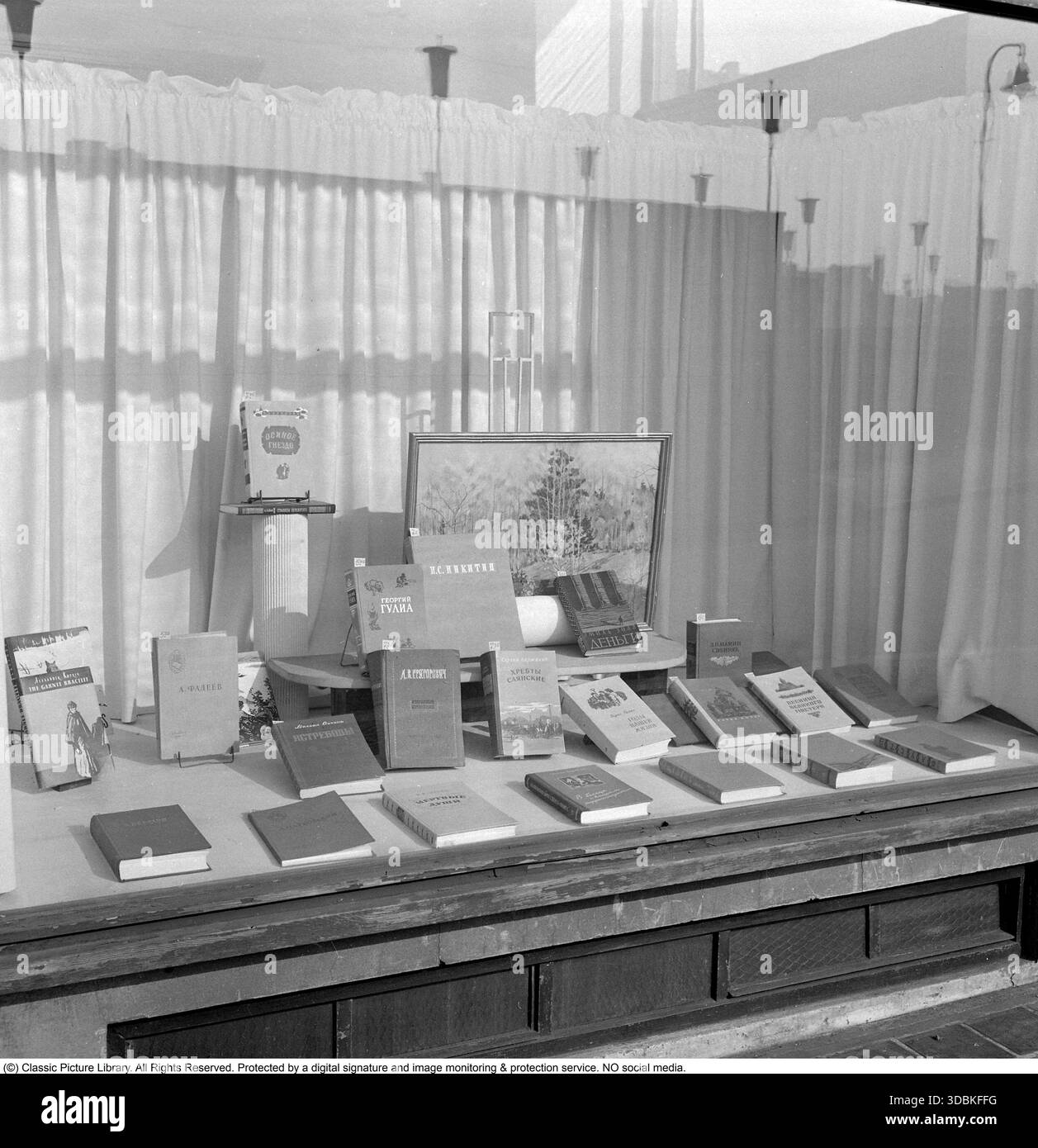 Russian Books in the Shop Window, Berlino Est (1957) questa foto del 1957 mostra una vetrina a Berlino Est che espone con orgoglio libri in lingua russa, uno spettacolo comune che promuove la letteratura e la cultura sovietica nel cuore della RDT. Negli anni '1950 della Repubblica Democratica tedesca, i libri russi (classici come Tolstoj o Gor'kij, più romanzi realisti socialisti e opere di propaganda) furono fortemente spinti attraverso le librerie statali e le esposizioni per promuovere l'amicizia con l'Unione Sovietica e l'allineamento ideologico. Stampati a basso costo in grandi tirature, erano strumenti per l'influenza culturale e l'istruzione, spesso prioritari Foto Stock