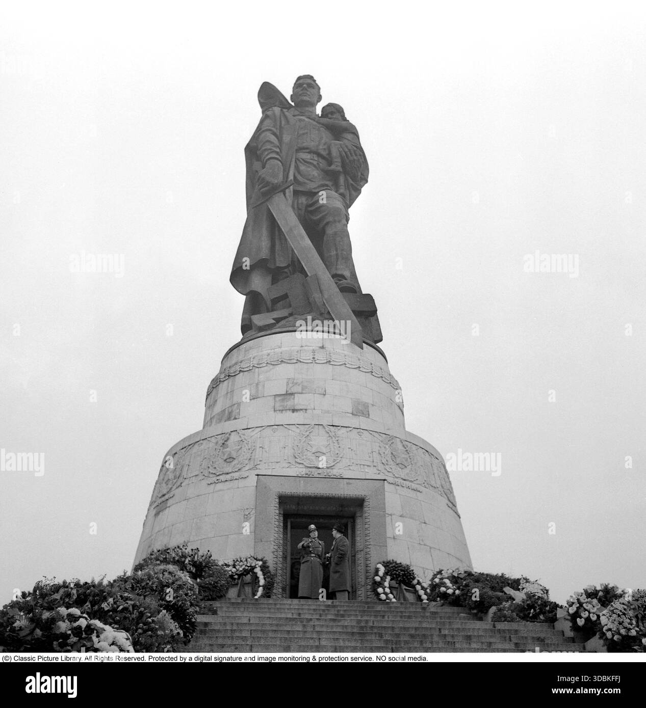 Memoriale di guerra sovietico, Treptower Park - Berlino Est (1957) questa impressionante foto del 1957 mostra la colossale statua di un soldato sovietico, ufficialmente intitolato "Liberatore e Salvatore di Berlino", che culla un bambino tedesco salvato mentre schiaccia una svastica sotto il suo stivale. Si trova nel cuore del vasto Memoriale di guerra sovietico nel Parco Treptower, Berlino Est. Inaugurato nel 1949, questo enorme complesso (uno dei tre più importanti memoriali sovietici a Berlino) onora i circa 80.000 soldati dell'Armata Rossa caduti durante la battaglia di Berlino nel 1945. Progettato in grande stile socialista-realista, presenta ampi prati Foto Stock