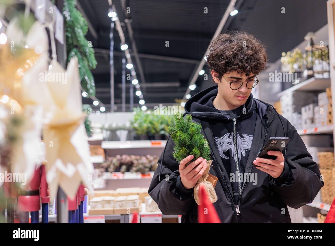 Adolescenti che acquistano decorazioni natalizie in negozio confrontando i prezzi su smartphone – vendita al dettaglio per le festività moderne e comportamento dei consumatori di generazione Z. Copyspace Foto Stock