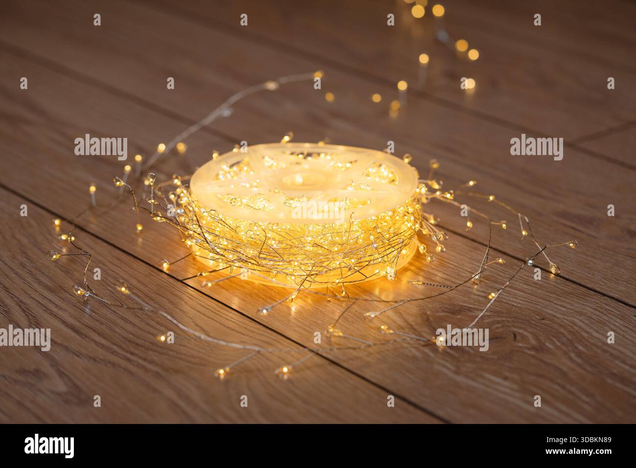 Decorazioni natalizie. Una bobina di calde luci a LED bianche che si illuminano delicatamente su un pavimento in legno. Alta risoluzione. Foto Stock
