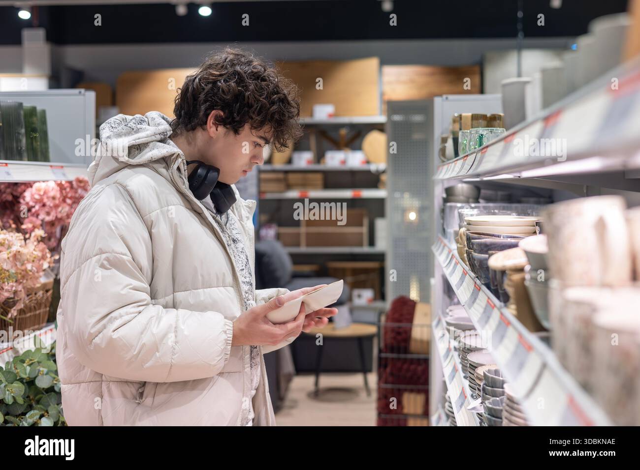 Teenager che sceglie stoviglie nel negozio di articoli per la casa – giovane cliente che sceglie la piastra nel corridoio degli utensili da cucina Foto Stock