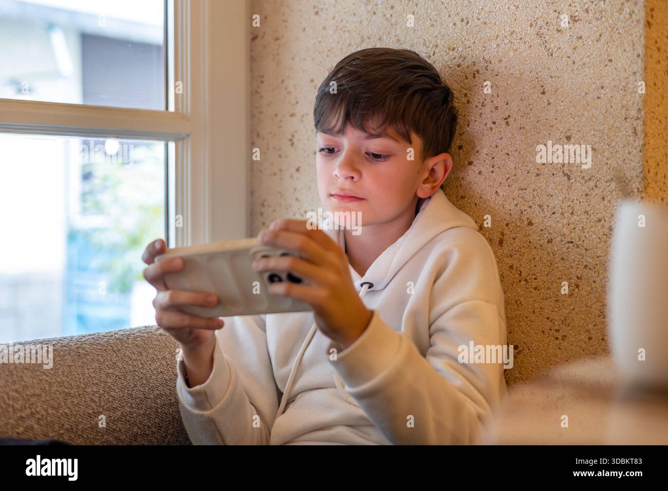 Ragazzo concentrato che gioca a videogame mobili su smartphone in interni, illustrando lo schermo, l'uso della tecnologia per l'infanzia e l'intrattenimento digitale a casa. Foto Stock