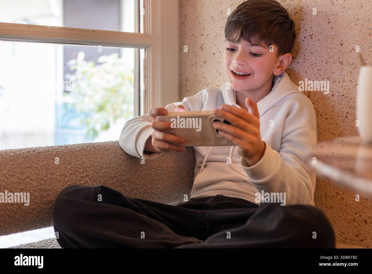 Ragazzo concentrato che gioca a videogame mobili su smartphone in interni, illustrando lo schermo, l'uso della tecnologia per l'infanzia e l'intrattenimento digitale a casa. Foto Stock