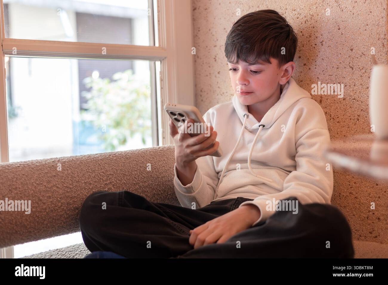 Bambini che guardano lo schermo dello smartphone all'interno, che rappresenta l'infanzia digitale, le comunicazioni online, lo schermo e la dipendenza tecnologica a casa. Foto Stock
