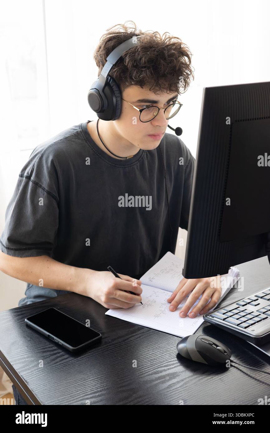 Teenager in cuffie per imparare la matematica online su computer Desk - studente concentrato che studia a casa con strumenti digitali, formazione remota e STEM Foto Stock