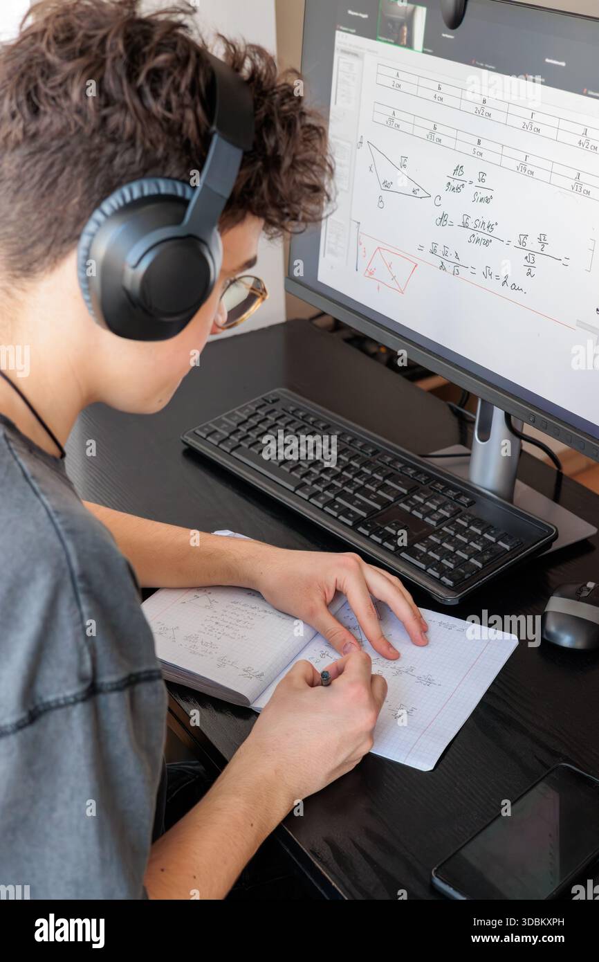 Teenager in cuffie per imparare la matematica online su computer Desk - studente concentrato che studia a casa con strumenti digitali, formazione remota e STEM Foto Stock