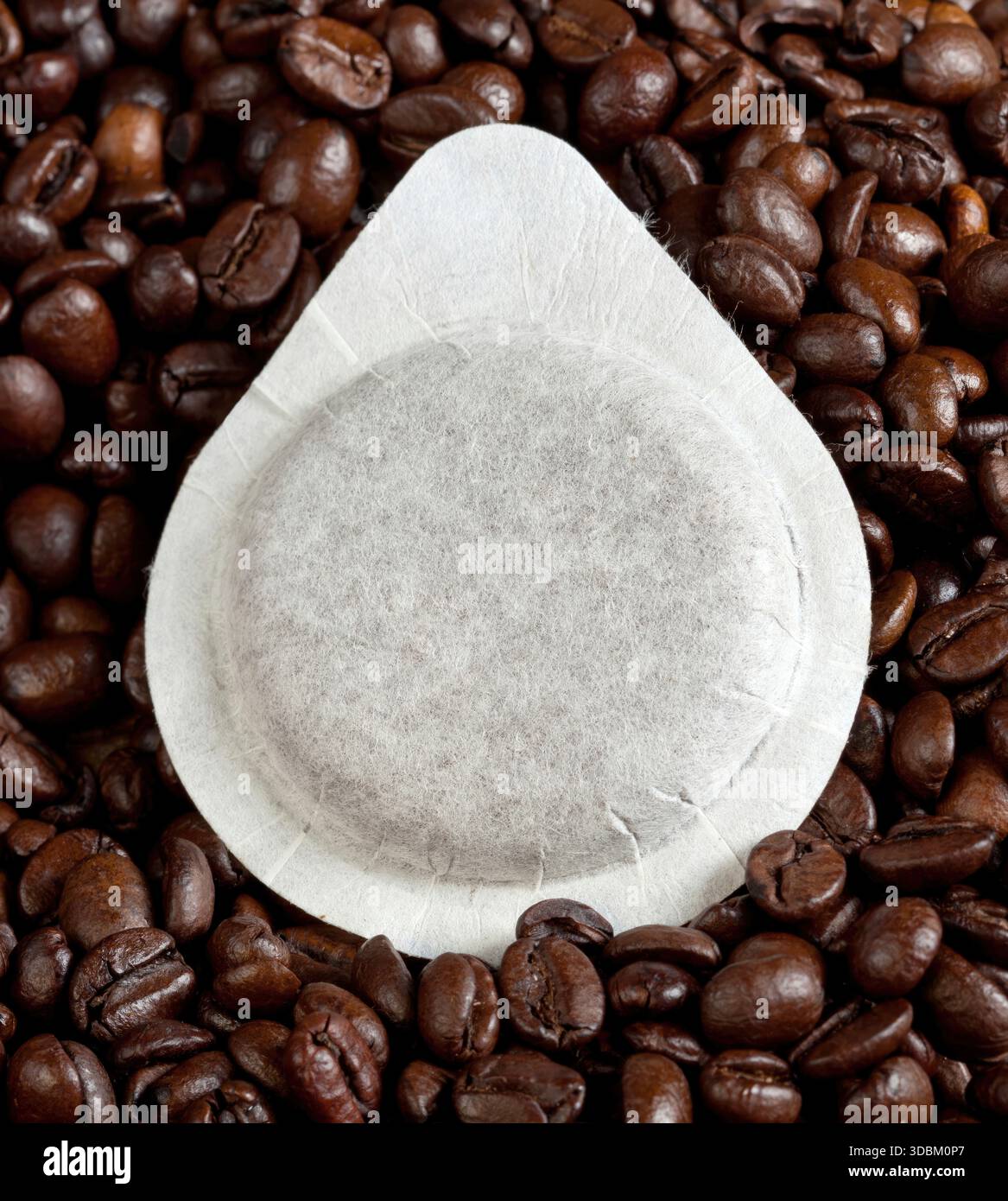 La cialda di caffè si appoggia sui chicchi tostati, creando consistenza e aroma. Le sfumature marroni si aprono su uno sfondo bianco, catturando l'essenza di una tazza perfetta per il mattino Foto Stock