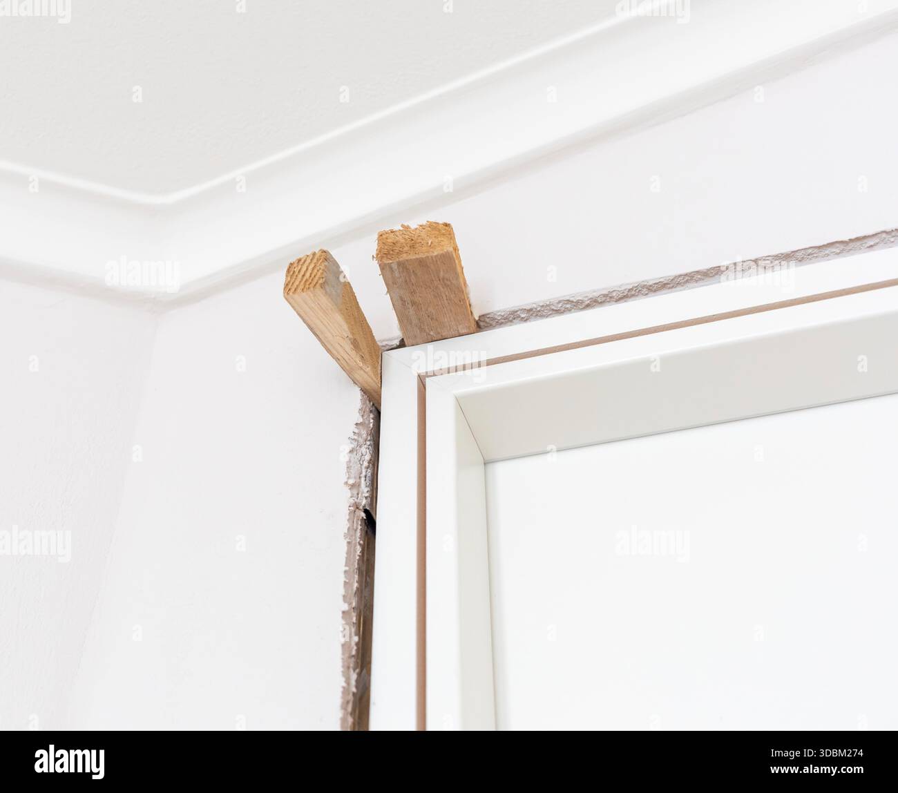 Due cunei in legno che sostengono un nuovo telaio bianco della porta durante i lavori di installazione e ristrutturazione in un appartamento, garantendo stabilità e precisione per una finitura impeccabile Foto Stock