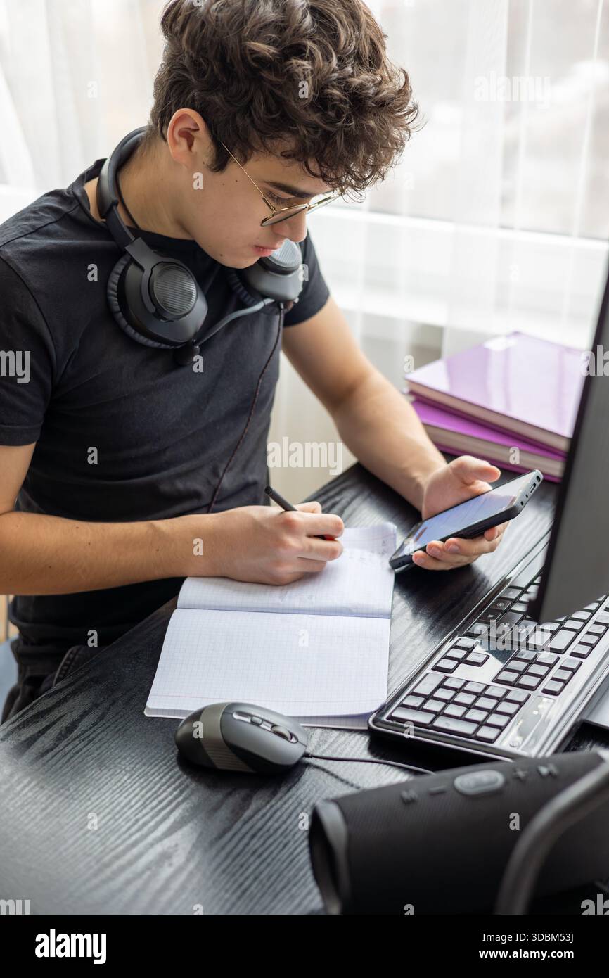 Adolescente che studia a casa con un computer. Teen freelance che lavora a un progetto a casa. Preparazione all'esame. Teen Boy che studia online. Foto Stock