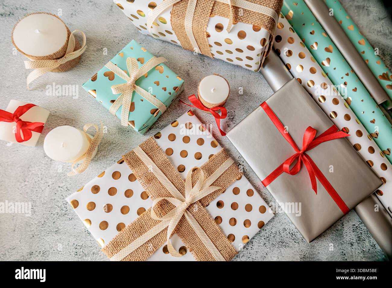 Elegante composizione natalizia con regali avvolti, candele decorative e dettagli dorati. Atmosfera calda e fatta a mano Foto Stock
