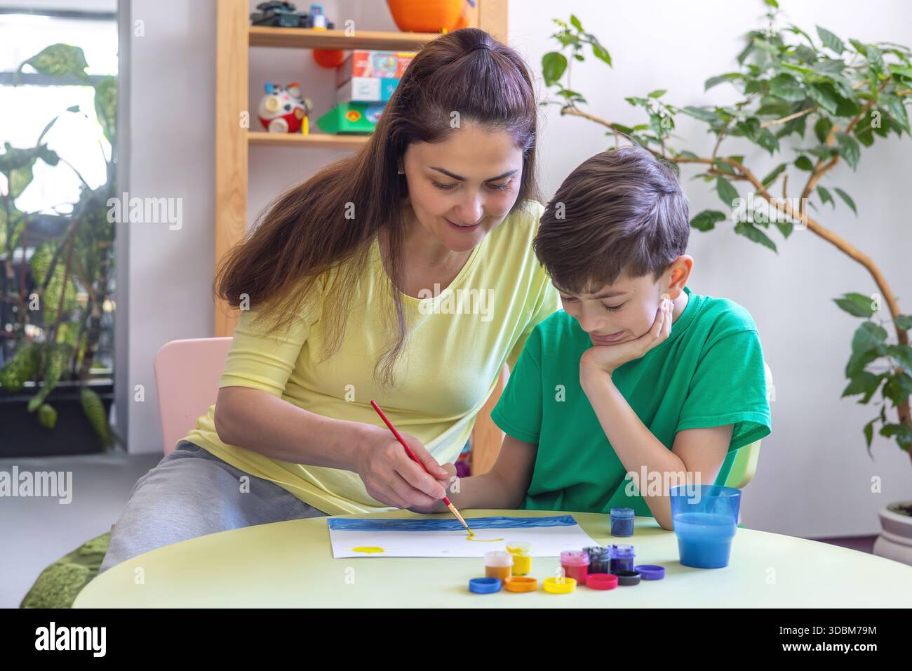 Sessione di Art Therapy: Pittura di adulti e bambini in un ambiente di supporto. Mamma aiuta suo figlio a disegnare a casa. Creatività, apprendimento, tempo in famiglia. Foto Stock
