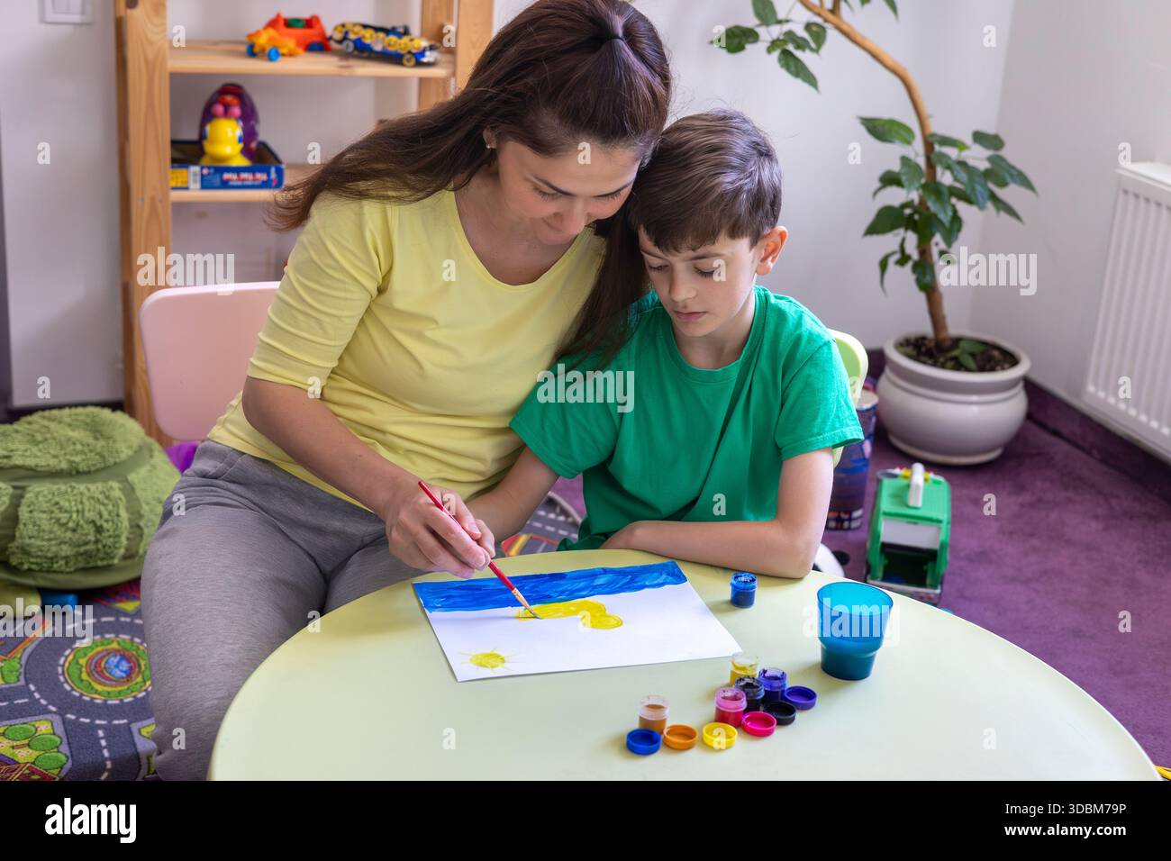 Sessione di Art Therapy: Pittura di adulti e bambini in un ambiente di supporto. Mamma aiuta suo figlio a disegnare a casa. Creatività, apprendimento, tempo in famiglia. Foto Stock