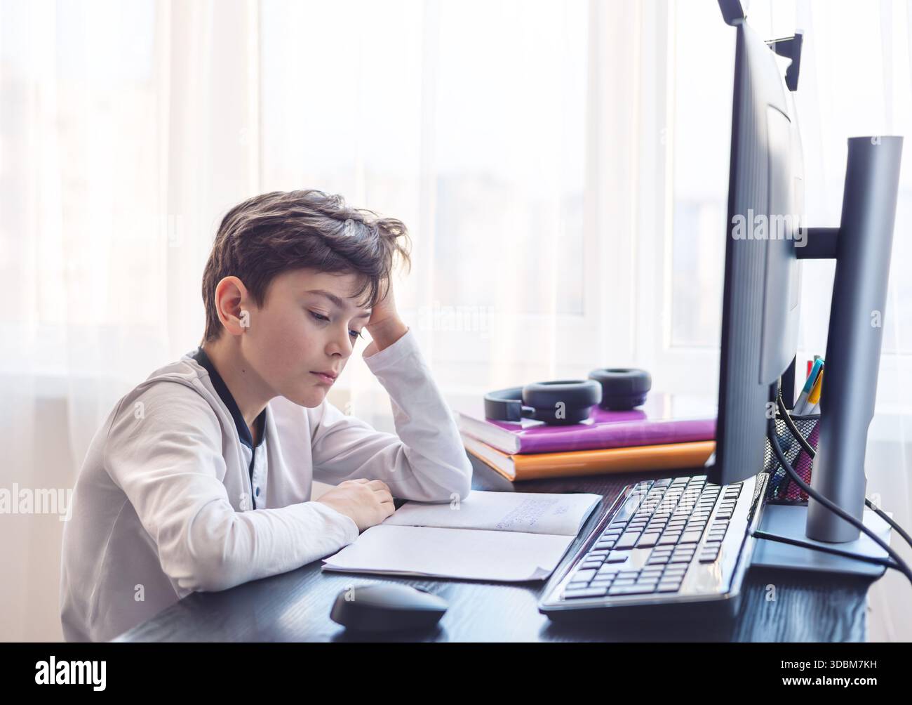 Frustrato studente di 7-9 anni tiene la testa tra le mani mentre studia al computer - problemi di concentrazione, sovraccarico digitale e difficoltà di apprendimento Foto Stock
