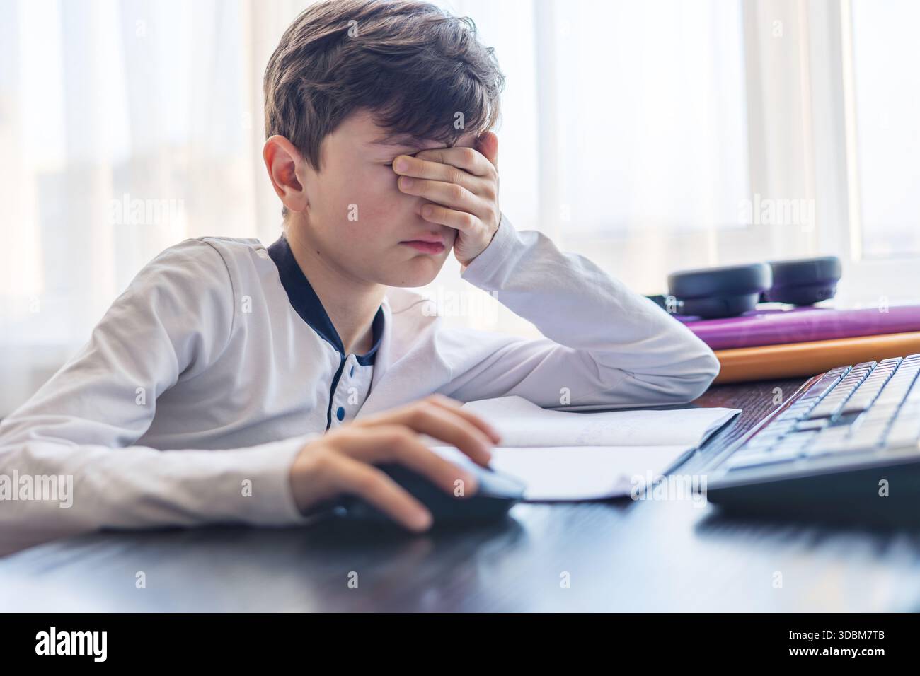 Frustrato studente di 7-9 anni tiene la testa tra le mani mentre studia al computer - problemi di concentrazione, sovraccarico digitale e difficoltà di apprendimento Foto Stock