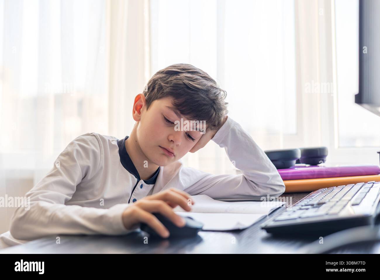 Frustrato studente di 7-9 anni tiene la testa tra le mani mentre studia al computer - problemi di concentrazione, sovraccarico digitale e difficoltà di apprendimento Foto Stock