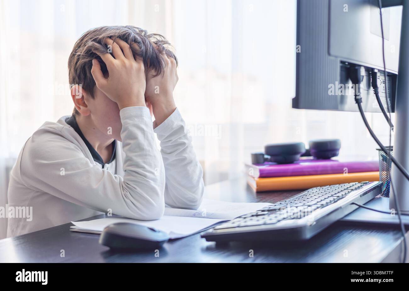 Frustrato studente di 7-9 anni tiene la testa tra le mani mentre studia al computer - problemi di concentrazione, sovraccarico digitale e difficoltà di apprendimento Foto Stock