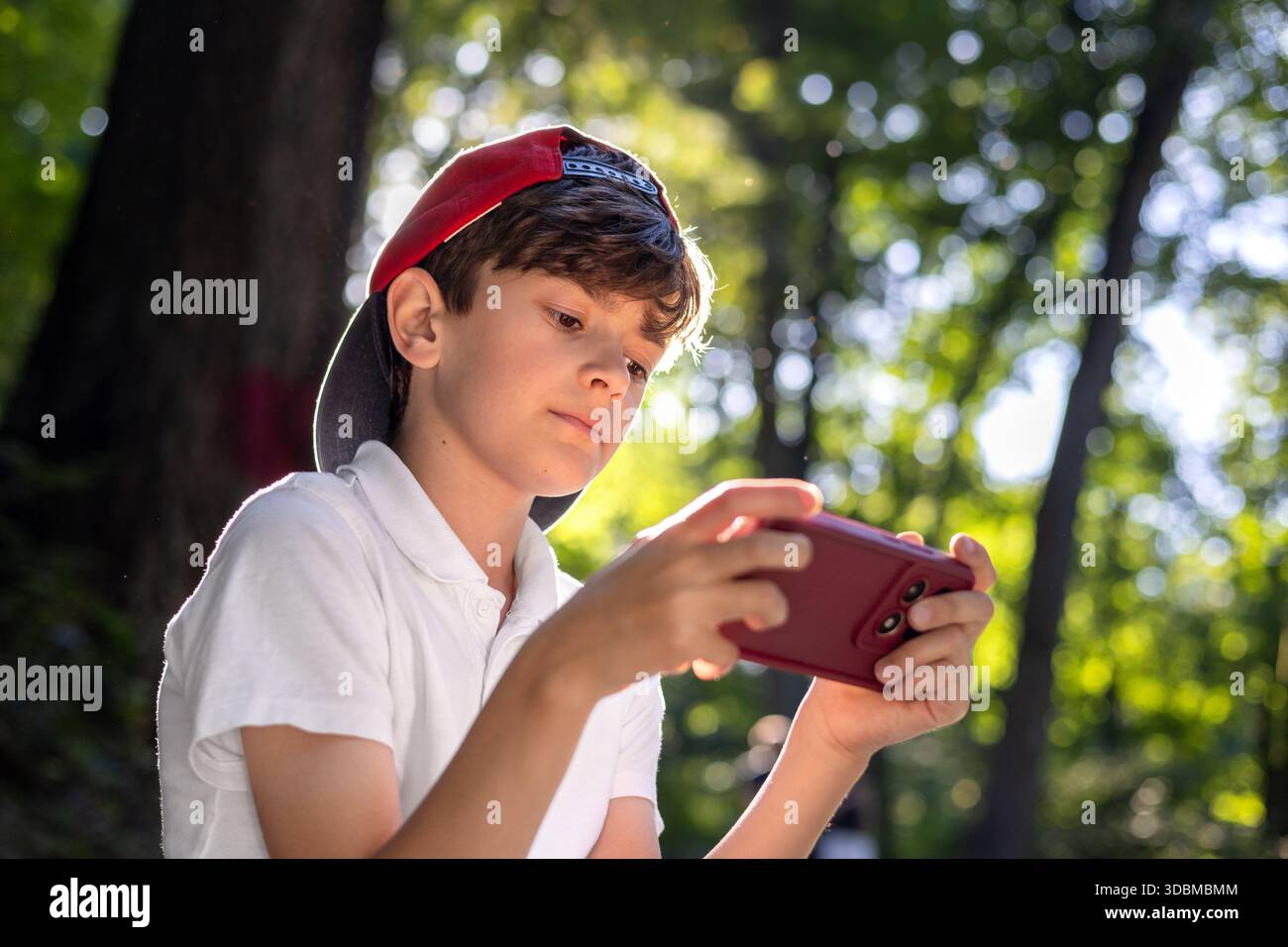 Bambino con smartphone nel parco, ragazzo che usa il telefono cellulare all'aperto, infanzia digitale, tempo dello schermo, dipendenza da tecnologia, bambini e gadget, social media, Foto Stock
