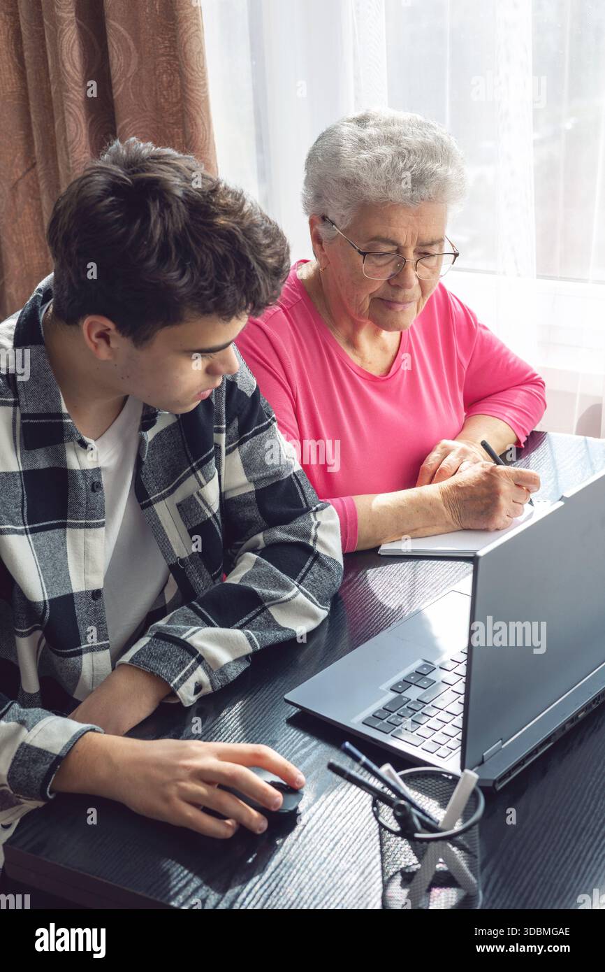 Nipote che aiuta la nonna con il computer, insegna le abilità digitali, le donne anziane imparano la tecnologia, il sostegno familiare, la comunicazione intergenerazionale Foto Stock