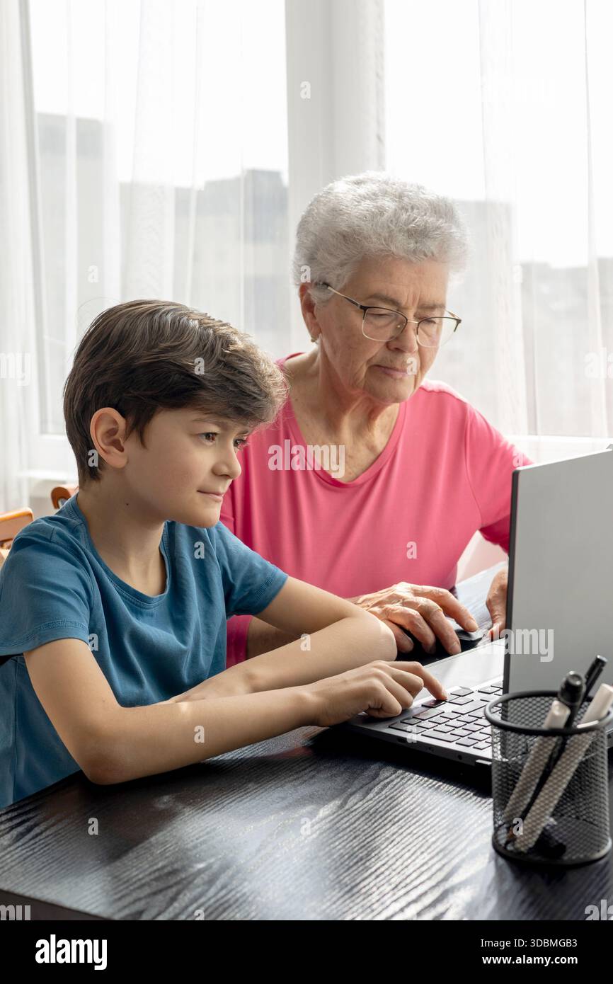 Nipote e nonna al portatile. L'aiuto del nipote nel padroneggiare il computer. Alfabetizzazione digitale degli anziani. Generazione alfa e baby boomer. Foto Stock