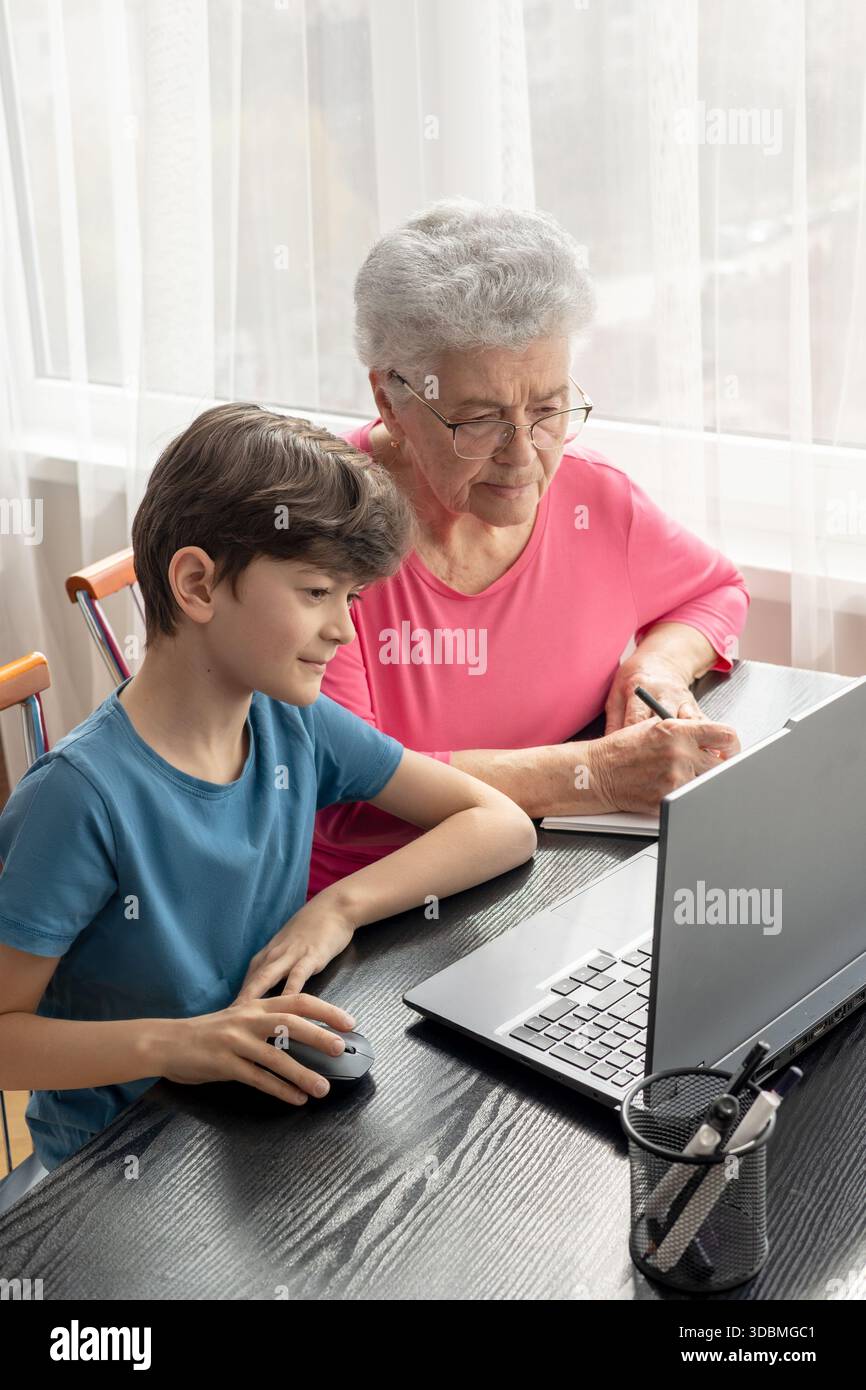 Nipote e nonna al portatile. L'aiuto del nipote nel padroneggiare il computer. Alfabetizzazione digitale degli anziani. Generazione alfa e baby boomer. Foto Stock
