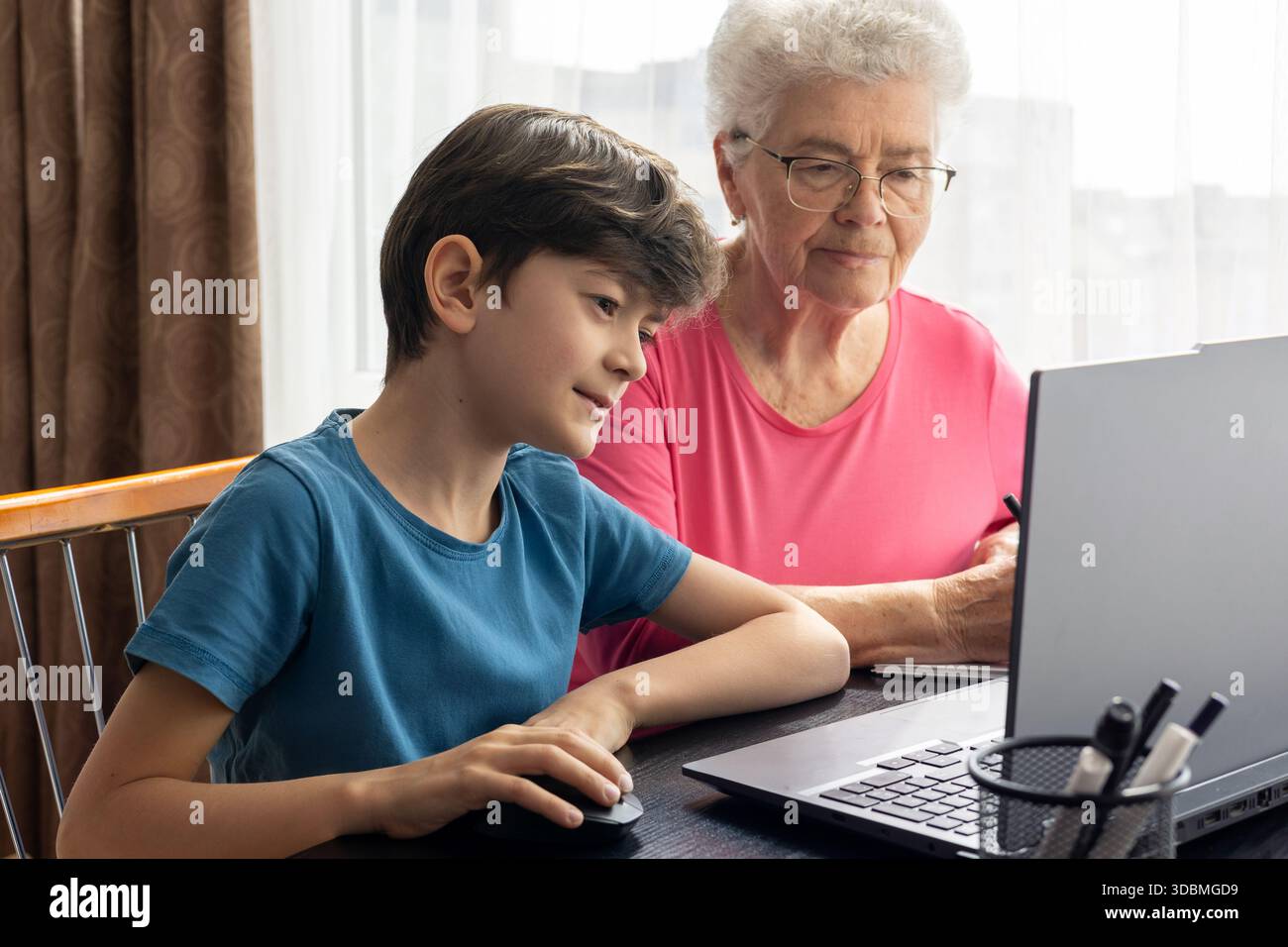 Nipote e nonna al portatile. L'aiuto del nipote nel padroneggiare il computer. Alfabetizzazione digitale degli anziani. Generazione alfa e baby boomer. Foto Stock