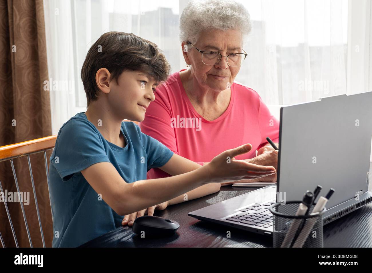 Nipote e nonna al portatile. L'aiuto del nipote nel padroneggiare il computer. Alfabetizzazione digitale degli anziani. Generazione alfa e baby boomer. Foto Stock