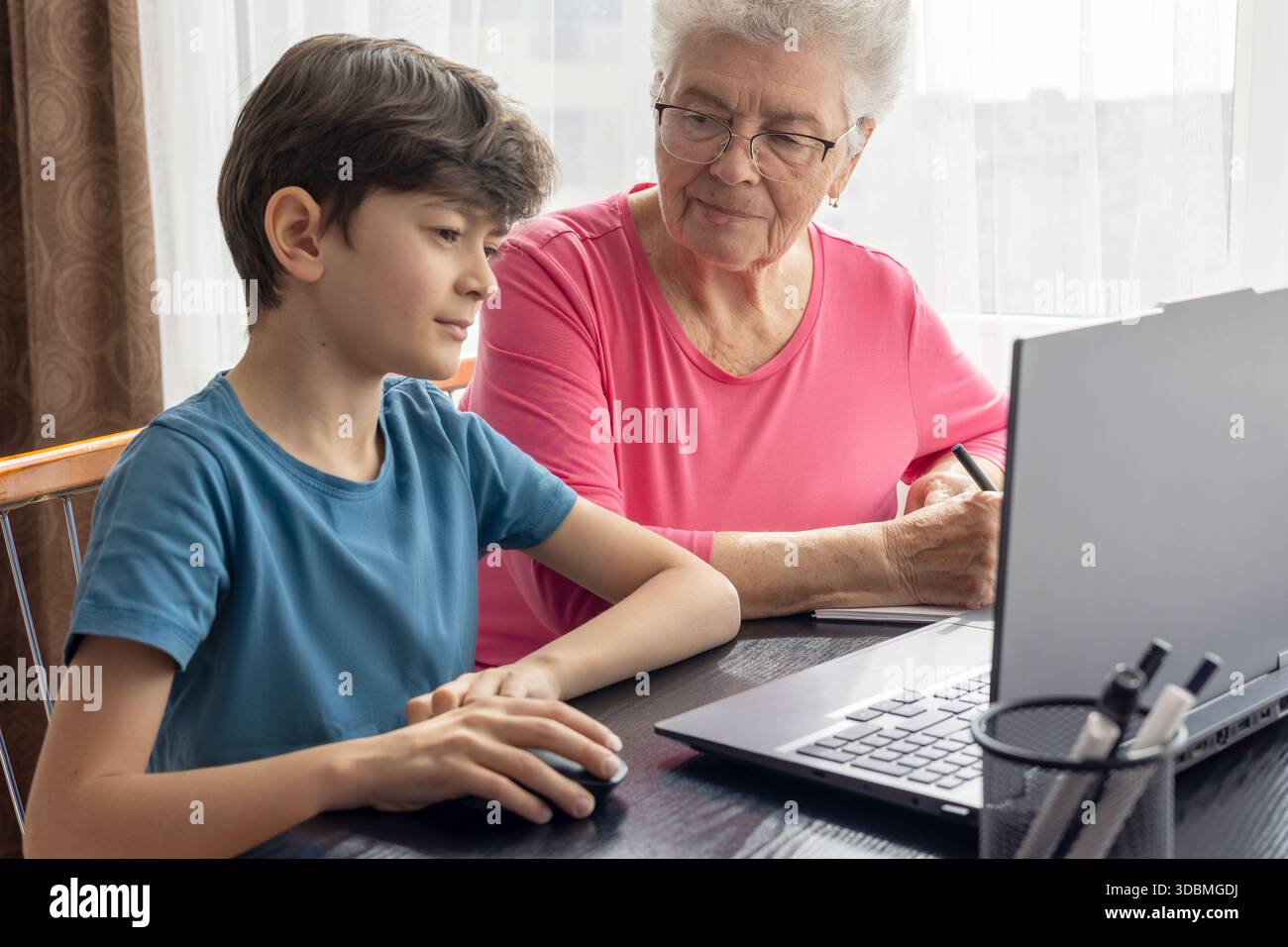 Nipote e nonna al portatile. L'aiuto del nipote nel padroneggiare il computer. Alfabetizzazione digitale degli anziani. Generazione alfa e baby boomer. Foto Stock
