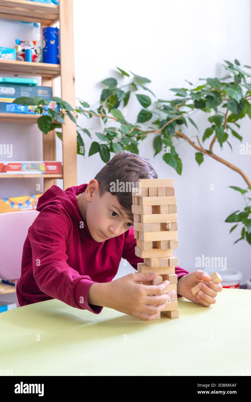 Il ragazzo gioca Jenga in un'accogliente stanza dei bambini. il tema dello sviluppo cognitivo, del pensiero logico, delle capacità motorie, della salute mentale, del supporto autistico Foto Stock