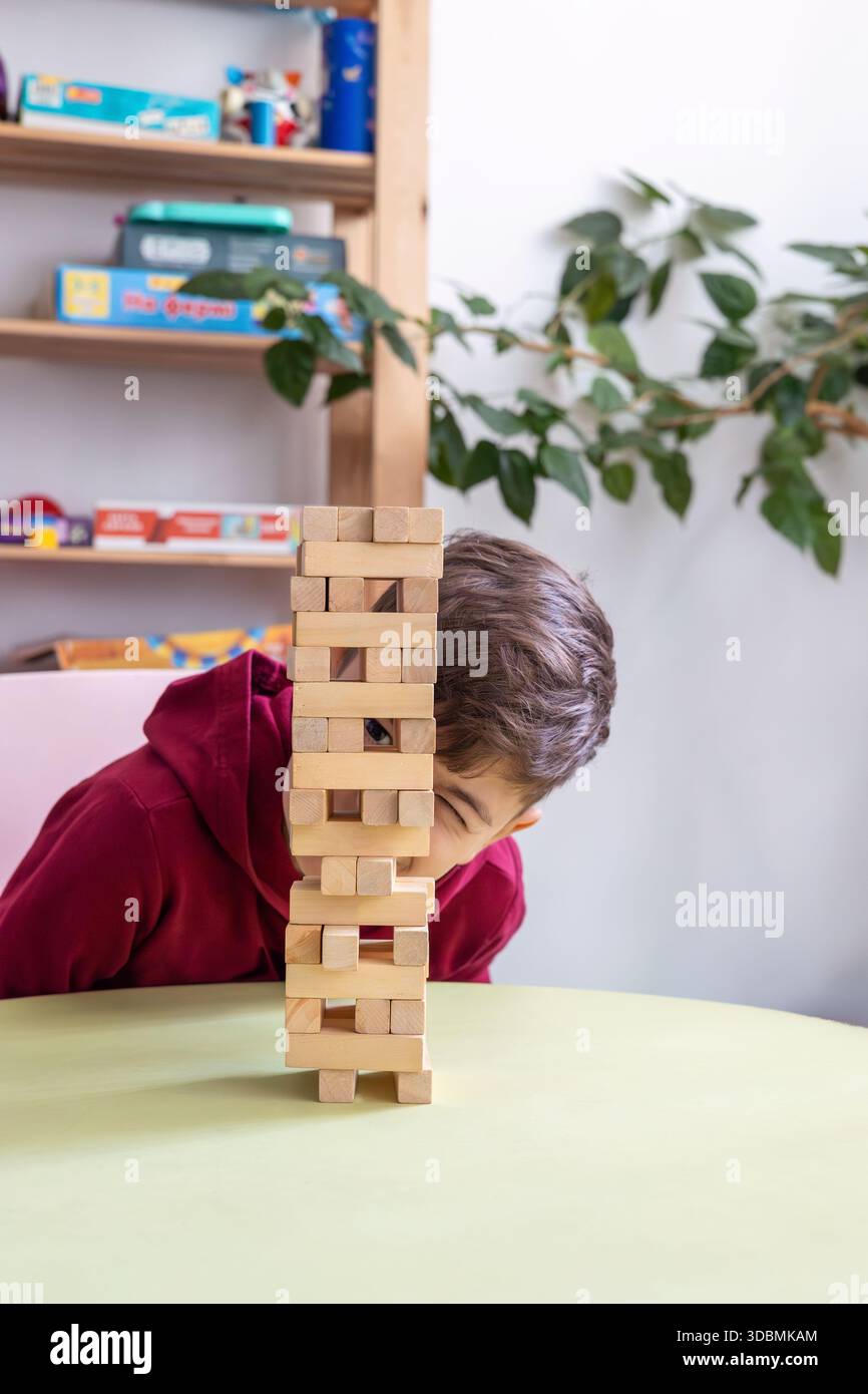 Il ragazzo gioca Jenga in un'accogliente stanza dei bambini. il tema dello sviluppo cognitivo, del pensiero logico, delle capacità motorie, della salute mentale, del supporto autistico Foto Stock