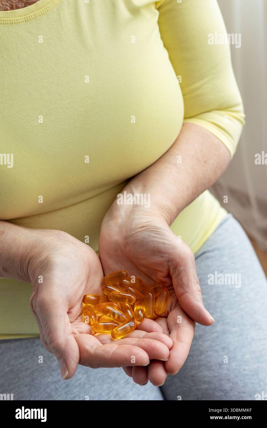Mani che invecchiano che tengono le capsule dorate. Salute in età adulta, mantenendo attività ed energia. Prevenzione delle malattie, uso di vitamine e integratori, trattamento Foto Stock