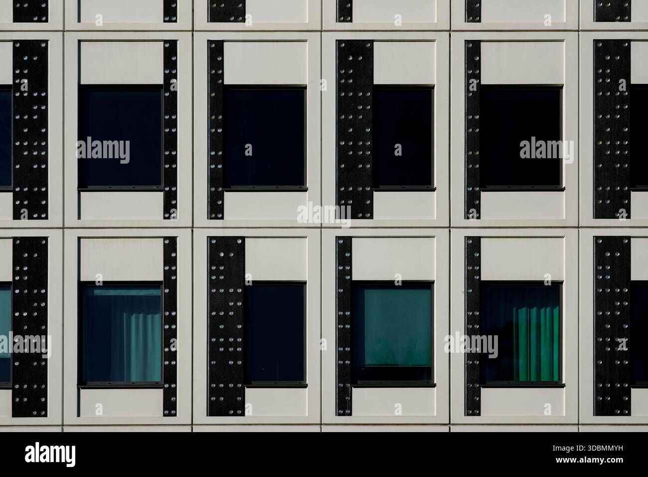 Simmetria strutturata: Ripetizione uniforme. Questa immagine mostra la facciata di un edificio per uffici a Stoccolma, Svezia. La disposizione a griglia delle finestre, incorniciata da pannelli in bianco e nero a contrasto, crea un senso di simmetria strutturata. Le finestre ai livelli inferiori sono parzialmente coperte da tende e tende, aggiungendo un elemento di variazione all'interno del modello uniforme. Foto Stock