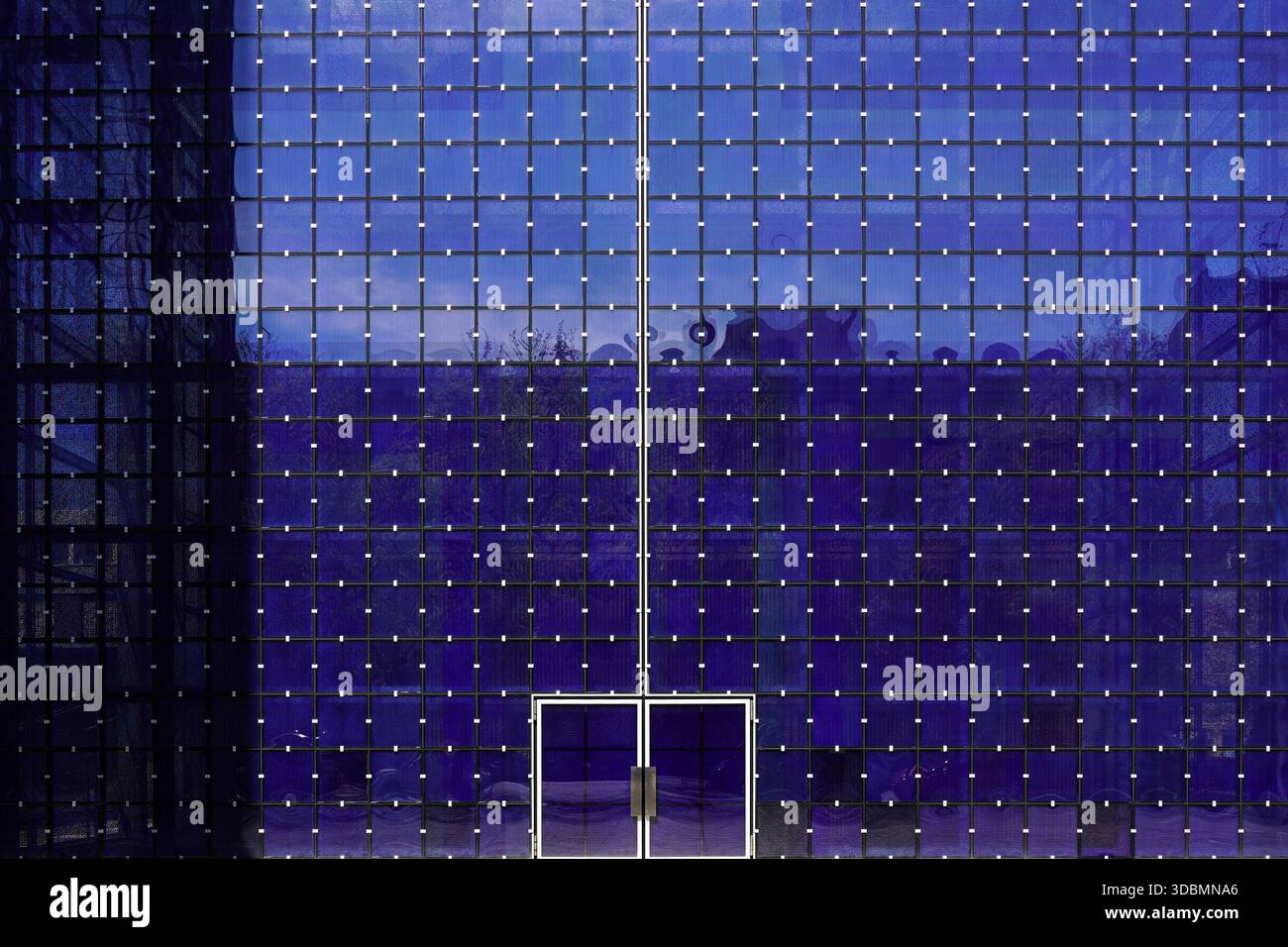 Monaco di Baviera, Germania, facciata d'ingresso della chiesa parrocchiale cattolica Herz Jesu a Monaco di Baviera Neuhausen, progettata da Allmann Sattler Wappner. La superficie in vetro con la sua struttura a griglia riflette l'area circostante, incorniciando la porta centrale all'interno di una suggestiva facciata blu, Foto Stock